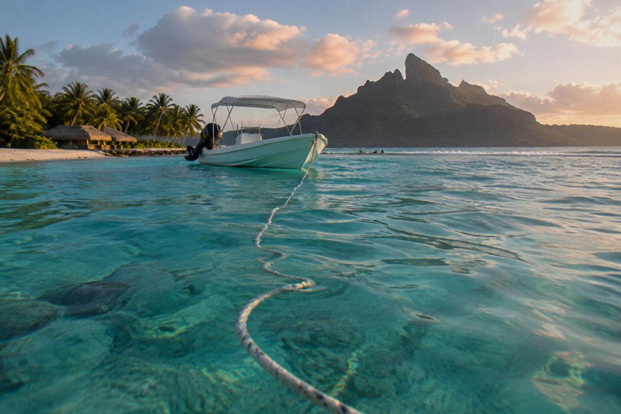 A small boat anchored over turquoise lagoon water beside a coral reef in Bora Bora