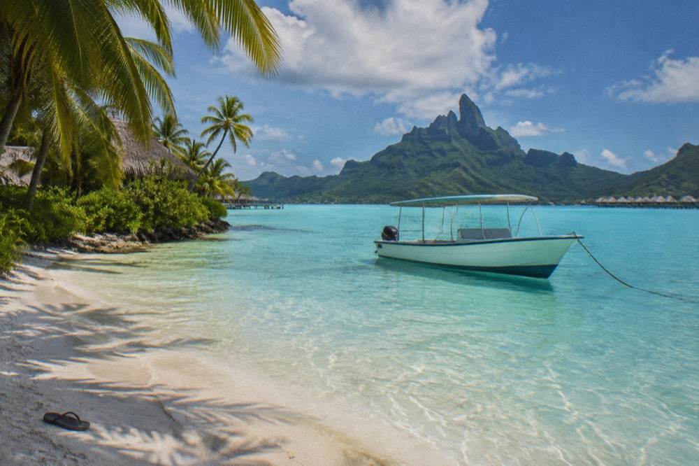 A small boat anchored beside a sandy motu islet in turquoise lagoon water