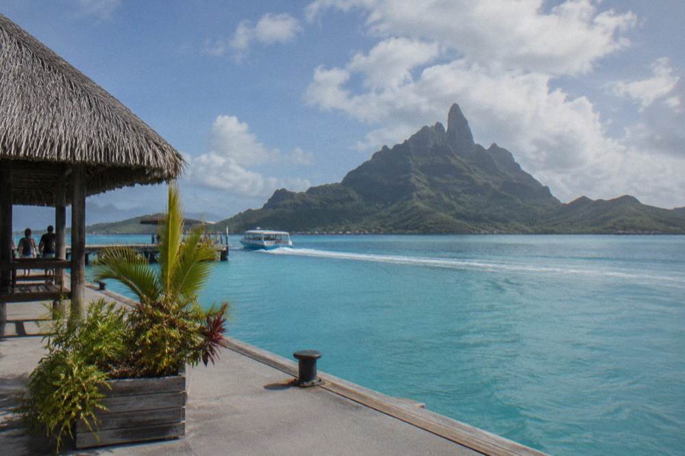 Mount Otemanu rising over calm turquoise lagoon water under scattered clouds